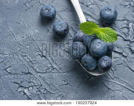 Freshly picked blueberries in spoon closeup. Ripe and juicy fresh blueberry with green mint leaves on textured concrete background. Bilberry on dark background with copyspace. Top view or flat lay