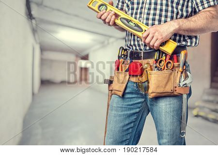 man with toolsbelt holding spirit level
