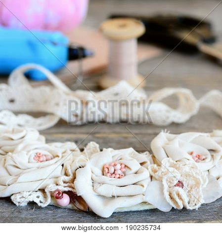 Mix materials flower necklace, glue hot gun, scissors, thread, felt on vintage wooden table. Summer beautiful fabric jewelry for women and girls. Idea of recycling fabric into stylish necklace