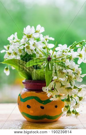 A bouquet of flowers birdcherry tree and grass forest in orange wooden pot, close-up