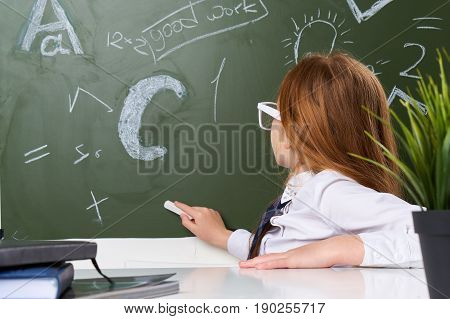 Girl schoolgirl knowledge, girl at the table wearing glasses at the blackboard.