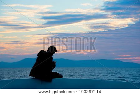 Silhouette of single man using mobile phone with sunset seascape background. Lonely people looking at smart phone outdoor reading message or using app. Travel and technology concepts. Copy space.