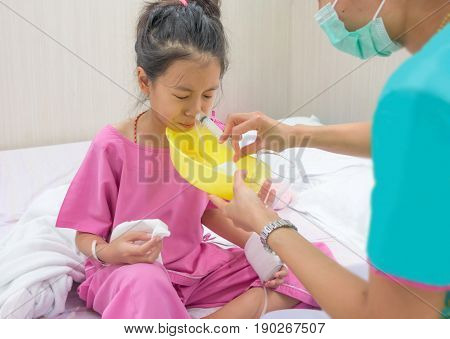 Ill young Asian girl with black hair sitting on bed in hospital. Sick kids cleaning nose with Nasal irrigation.