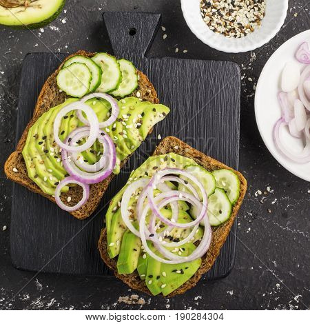Sandwiches on toast grain dark bread with slices of avocado, sweet pink onions and multi-colored sesame seeds. Top view.