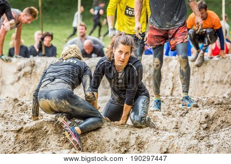 Stockholm Sweden - June 03 2017: Close up view two young caucasian woman struggling in a mud obstacle to complete the course of the annual event Toughest Stockholm. People in the background.