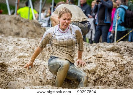 Stockholm Sweden - June 03 2017: Close up front view one caucasian woman struggling in an mud obstacle to complete the course of the annual event Toughest Stockholm. People in the background.