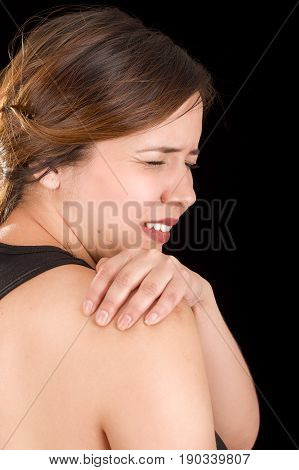 Close up of a beautiful young woman suffer from shoulder pain in a black background.