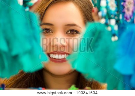 Close up of a smiling woman hiding behind a magenta catchdreamer, in colorful market background