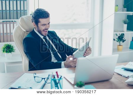Cheerful Young Businessman Is Plying A Game On His Tablet In Office. He Is Very Excited, Wearing For