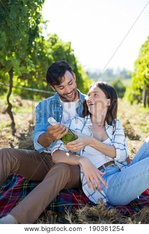 Happy couple holding winebottle while sitting at vineyard