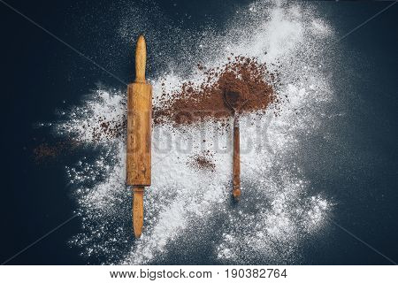wooden rolling pin with flour and a spoon of cocoa on a black and blue background. Concept: creative chaos