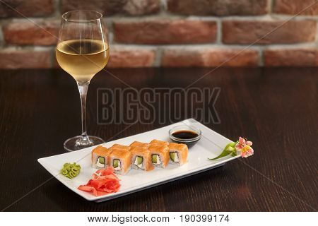 Philadelphia maki sushi rolls with salmon cheese cream cucumber on white plate and glass of wine