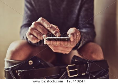 closeup of a young caucasian man using his smartphone in the toilet while sitting in the bowl