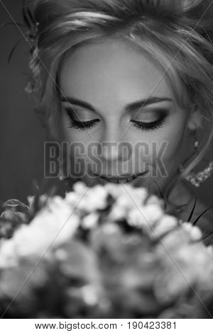 Happy beautiful bride with bright make-up and voluminous hairdress looks at her bright bouquet and smiles black and white frame