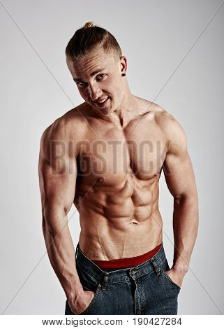 Young handsome guy with naked sexy torso posing in studio over gray background.
