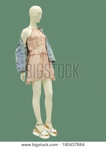 Full-length female mannequin dressed in blue jeans jacket and pink dress. Isolated on green background. No brand names or copyright objects.