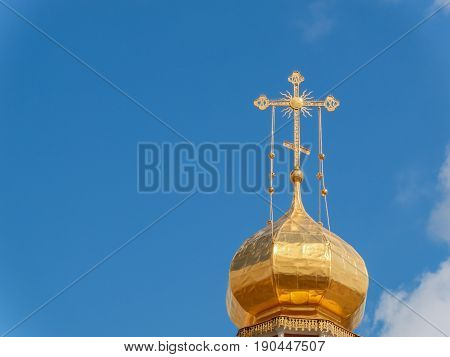 The Golden dome of an Orthodox temple on background of blue sky and clouds. Golden cross on the dome of the temple.