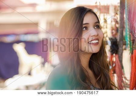 Close up of a beautiful smiling young woman looking a colorful andean traditional art, in colorful market fabrics background.
