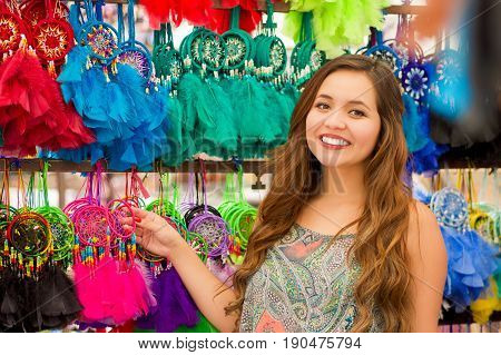 Close up of a beautiful smiling young woman touching a colorful catchdreamers, in colorful market fabrics background.