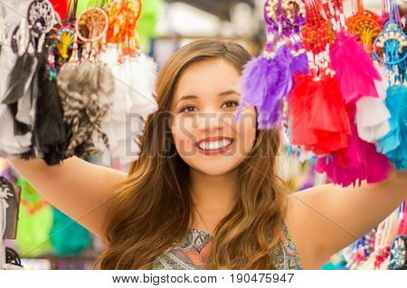 Close up of a beautiful smiling young woman hiding behind a colorful catchdreamer, in colorful market fabrics background.