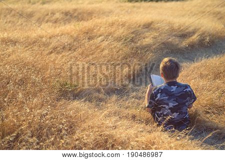Boy reading book in yellow grass high in the hills, watching beautiful sunset above Bay Area, rear view. Can be used as header.
