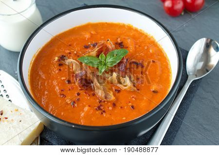 Thick tomato soup with basil and fried bacon in a black ceramic bowl on a grey abstract background. Healthy eating concept Fresh tomato soup with creme fraiche