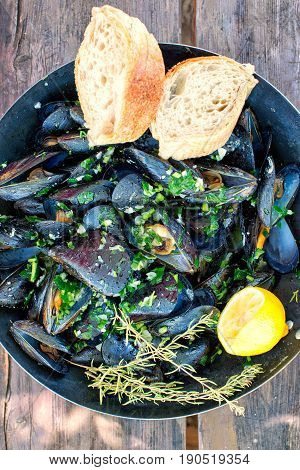 gourmet mussels served on a pan and a wooden plank with fresh herbs for a tasty seafood meal