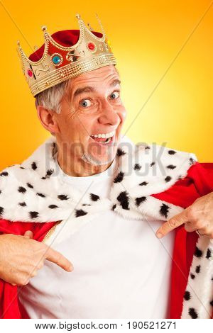 senior man wearing a king's robe and crown, pointing at his white t-shirt