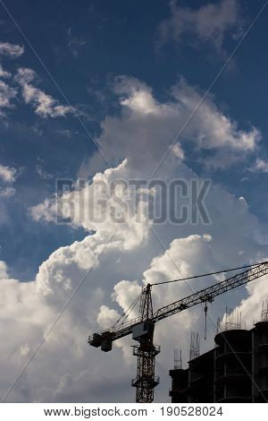 silhouette of high construction crane build unfinished city housing against the background of the blue sky and clouds