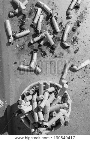 Ashtray full of cigarette stubs and some of them outside the tray
