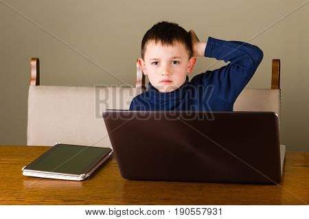 Cute little boy on new technology sitting behind a laptop and tablet pc at home looking concentrated.