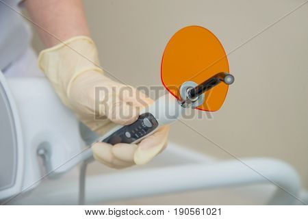 Hand in medical glove holding Dental UV curing light. Ultraviolet polymerization Lamp with orange blocking glass.