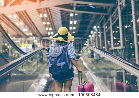 Young woman traveler in international airport with backpack holding suitcase or baggage in her hand Beautiful young tourist girl with backpack and carry on luggage in airport terminal on travelator