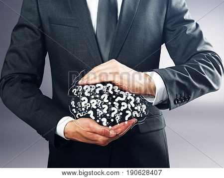 Businessman holding pile of drawn question marks on grey background. FAQ concept