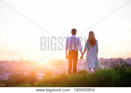 Young Couple Is Holding Hands On A Background Sunset