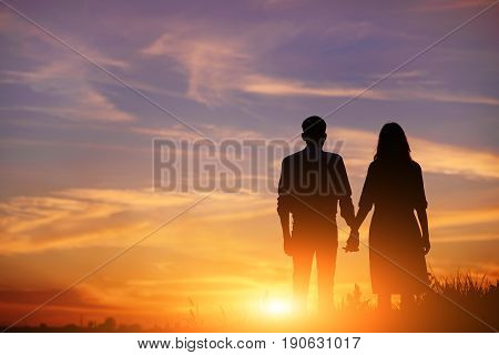 Young Couple Is Holding Hands On A Background Sunset Silhouette