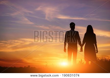 Young Couple Is Holding Hands On A Background Sunset Silhouette