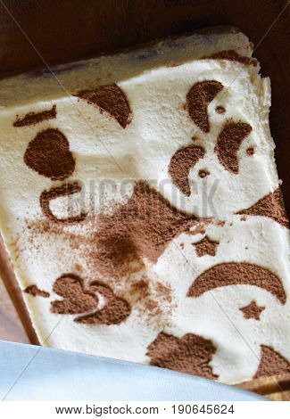 tiramisu decorated with drawings stencil of cocoa on a dark wooden Board
