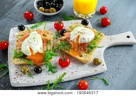 Poached egg on grilled toast with smoked salmon, rucola, olives, vegetables and orange juice. on white board. healthy breakfast.