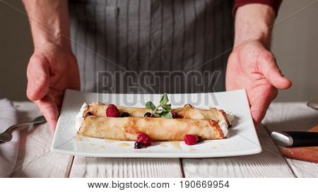 Chef serving plate. Cottage cheese pancake roll in restaraunt. Untecognizable male cook show prepared meal on white plate.