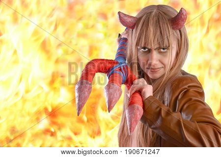 Girl in the guise of a devil with a trident on the background of fire