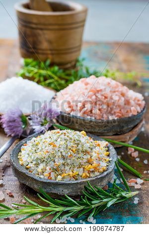 Different types of natural salt in stone bowls on wooden surface. White sea salt pink Himalayan salt Spiced salt with rosemary