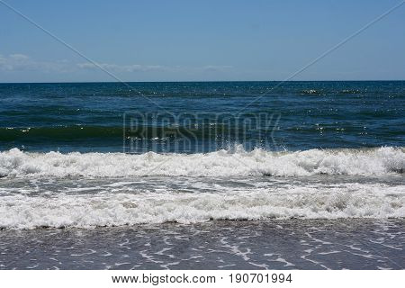 The beach with the ocean waves breaking and leaving the white foam behind and the blue waters beyond.