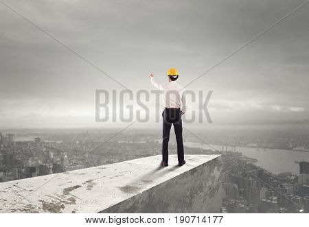 Businessman with helmet indicates the right direction on the roof above the city