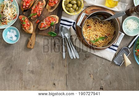 Italian dinner table with pasta and bruschetta on light rustic wooden table top view