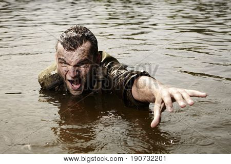 Wet and dirty soldier in uniform overcomes river