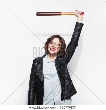 Young pretty stylish girl in leather jacket and glasses holding batt above head and looking at camera.