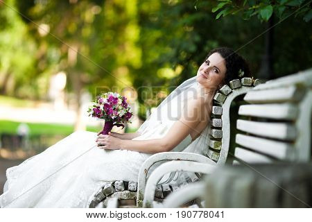 Sweet bride rests on white bench in the park