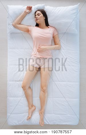 Pleasant relaxation. Attractive peaceful pretty woman having a nap and enjoying it while feeling comfortable on her bed