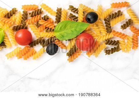 Pasta salad ingredients on white marble with a place for text. Rotini, cherry tomatoes, fresh basil leaves, and black olives